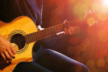 Young man playing on acoustic guitar on dark background with light effect