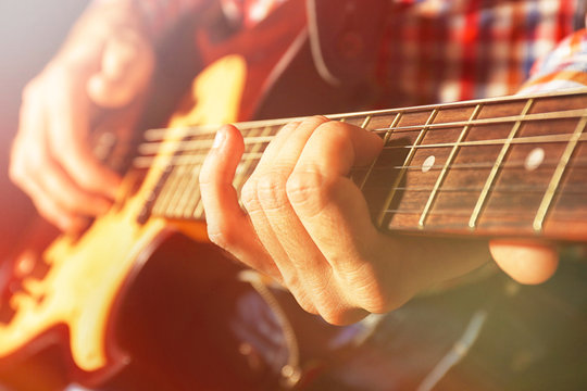 Young man playing on electric guitar on dark background with light effect