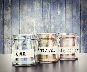 Three jars for different needs full of banknotes on wooden background