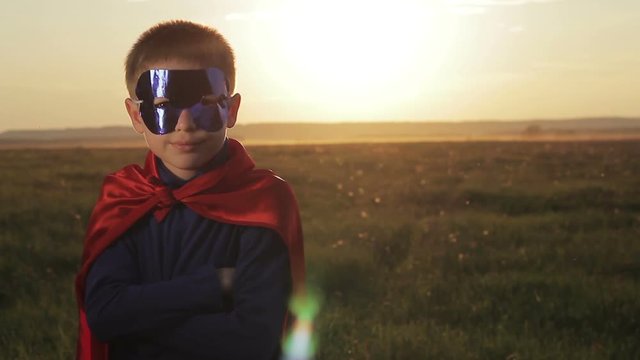 Boy dressed with a Superman cape running in a field, looking into the sunset