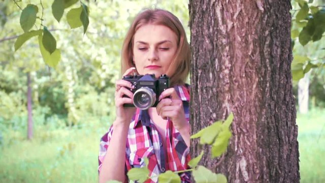 Beautiful young girl looks out from behind a tree and taking pictures. Slow motion