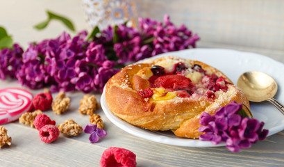 Freshly baked bun wiyh strawberry on wooden table wiyh lilac in spring time in sunny day
