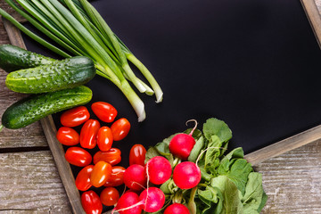 Background of blank black color with fresh healthy vegetables, green onion, radish, cucumber, tomatoes. Empty space for text. Top view.