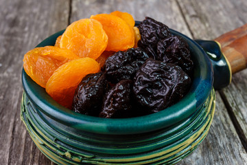 Organic prunes, dried plums and dried apricots in old tableware on rustic table