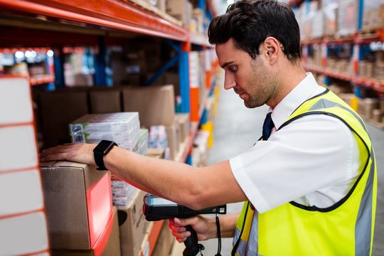 Warehouse manager with yellow coat scanning barcode on box 