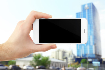 Hand shows mobile smart phone, urban city blurred background