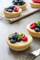 Delicious tartlets with raspberries and blueberries on a rustic wooden table
