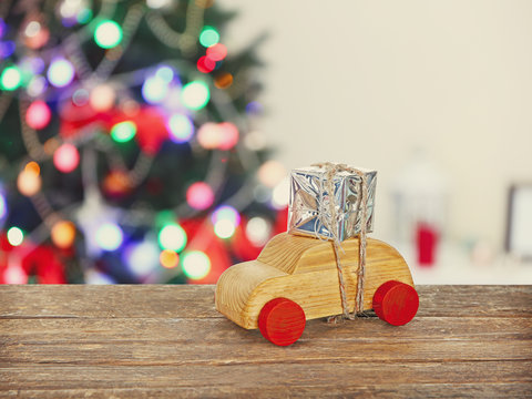 Wooden toy car carrying Christmas miniature gift on shiny lights background
