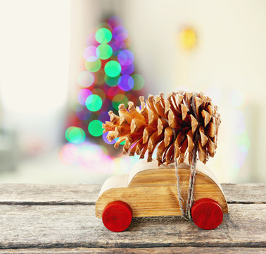 Wooden toy car carrying Christmas pine on shiny lights background