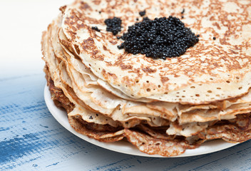 Pile of pancakes with black caviar on top on white plate