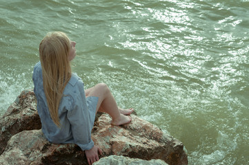 Девушка в рубашке сидит на камнях