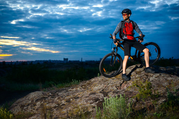 Cyclist Resting with Mountain Bike on the Rock at Sunset