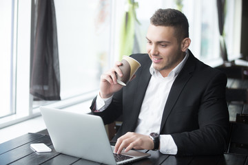 Portrait of young cheerful businessman working at wooden table i