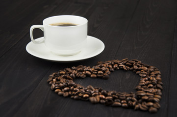 White cup of coffee with coffee beans as a heart on a wooden table
