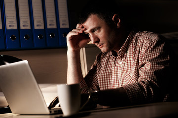 Young businessman working late on laptop at night in dark office
