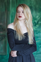 Fototapeta premium Elegant blonde in a black dress near grunge wall
