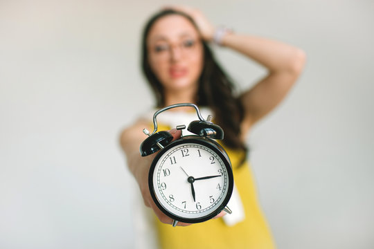 Young woaman holding alarm clock horrified about deadlines