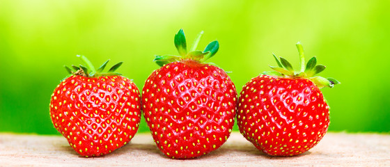 Three ripe, organic strawberry on blurred green background