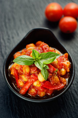 Vegan food, chickpeas stewed with tomatoes and peppers on black background