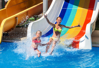 Two children on water slide at aquapark show thumb up. Summer swimming holiday. There are two water slides in aqua park. Swimming outdoor. - 112872953