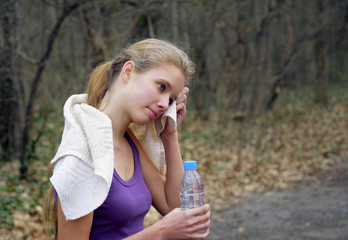 Fototapeta premium Sport girl runner is jogging on forest stop and drink of bottle water path in park.