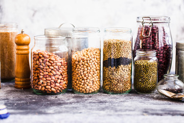 Collection of grain products, lentils, soybeans and red beans in storage jars over on kitchen rural table.