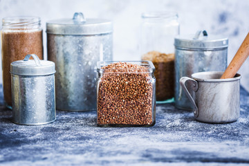 Buckwheat cereal glass jar and variety metallic storage jars on a kitchen country table.