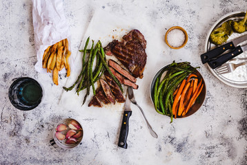 Dinner food tabletop. Overhead of Bbq fillet steak sliced with potatoes, carrot, green beans fries on a grey table.