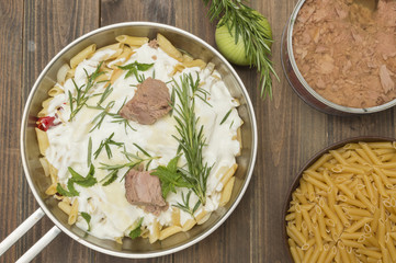 macarrones con nata y atun, decorados con hojas de romero, cuenco con macarrones sin cocer