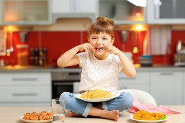 Adorable little girl eating spaghetti sitting on table