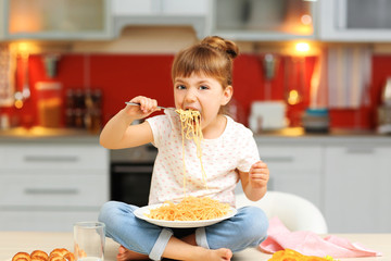 Adorable little girl eating spaghetti sitting on table