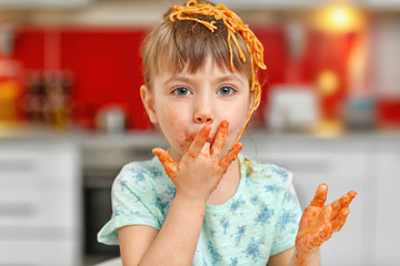 Adorable little girl eating spaghetti in kitchen