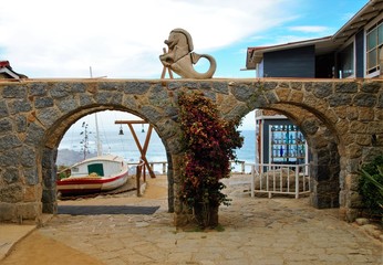 View through an arch onto a white boat, a wooden structure with green bells and the ocean