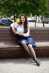 Young beautiful girl sitting on a bench in the summer park