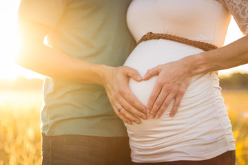 A pregnant woman with a guy folded heart with hands on belly