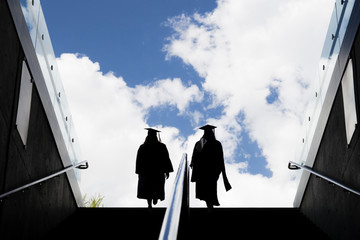 Silhouette of two students in a robe climb up the stairs