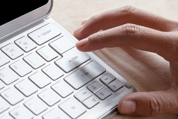 Close-up of male forefinger on button of silver color keyboard on tablet computer., on a wooden table under morning sunlight.