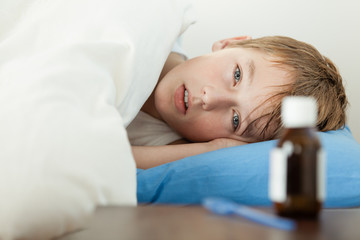 Feverish boy under thick blanket beside medicine