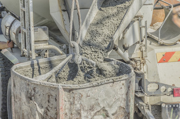 Concrete mixer truck pouring liquid concrete into the tower crane bucket at the construction...