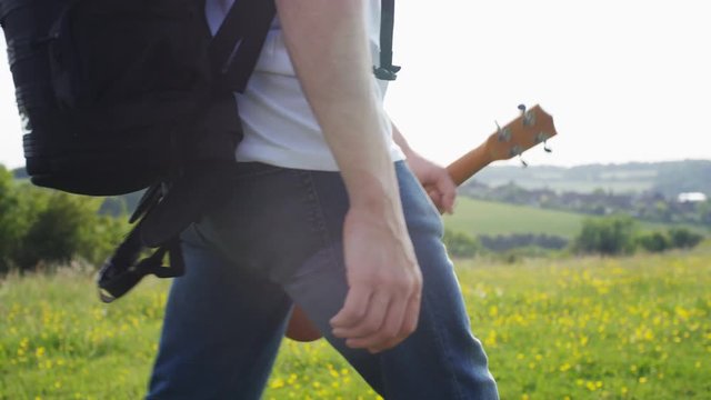 4K Musician holding a small guitar walking in nature, in slow motion