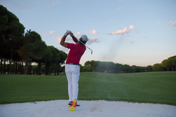 golfer hitting a sand bunker shot on sunset