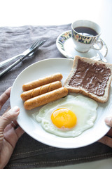 Woman's hands holding plate of breakfast with egg, sausages, bre