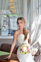 Beauty bride in bridal gown with bouquet and lace veil indoors. Beautiful model girl in a white wedding dress. Female portrait of cute lady. Woman with hairstyle