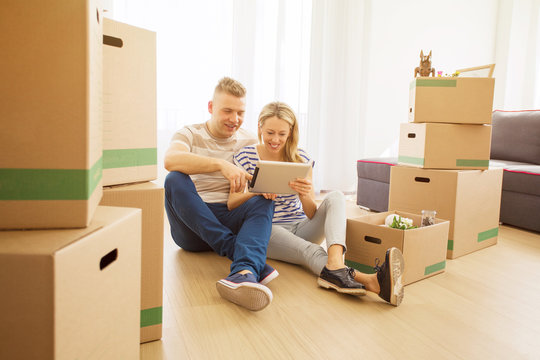Couple surrounded with moving boxes looking at tablet