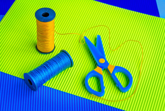 Sewing spools of blue and yellow caprone threads, plastic scissors on colorful corrugate paper