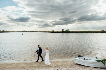 Fototapeta na wymiar Bride and groom walking near the boat at river