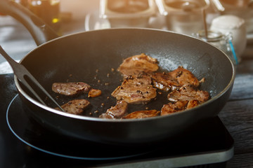 Pieces of meat on pan. Frying pan with brown meat. Veal medallions with whole pepper. Preparation of high-calorie dish.