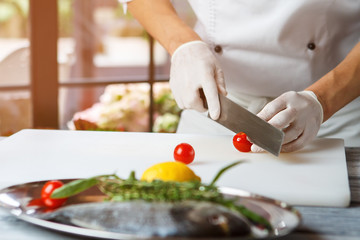 Hands with knife cut tomato. Small tomatoes on cooking board. Restaurant chef prepares food. Juicy cherry tomatoes.