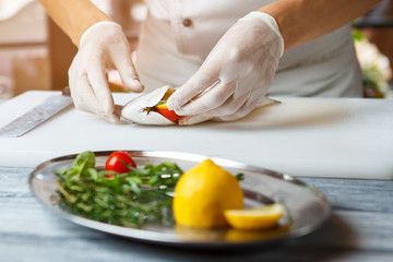 Hands put lemon into fish. Fish on white cooking board. Chef stuffs fish with lemon. Preparing a healthy seafood dish.