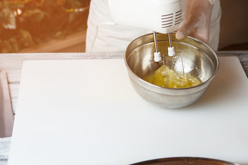 Hand beating eggs with mixer. Bowl with raw egg. Chef prepares delicious omelet. Fresh product rich in nutrients.